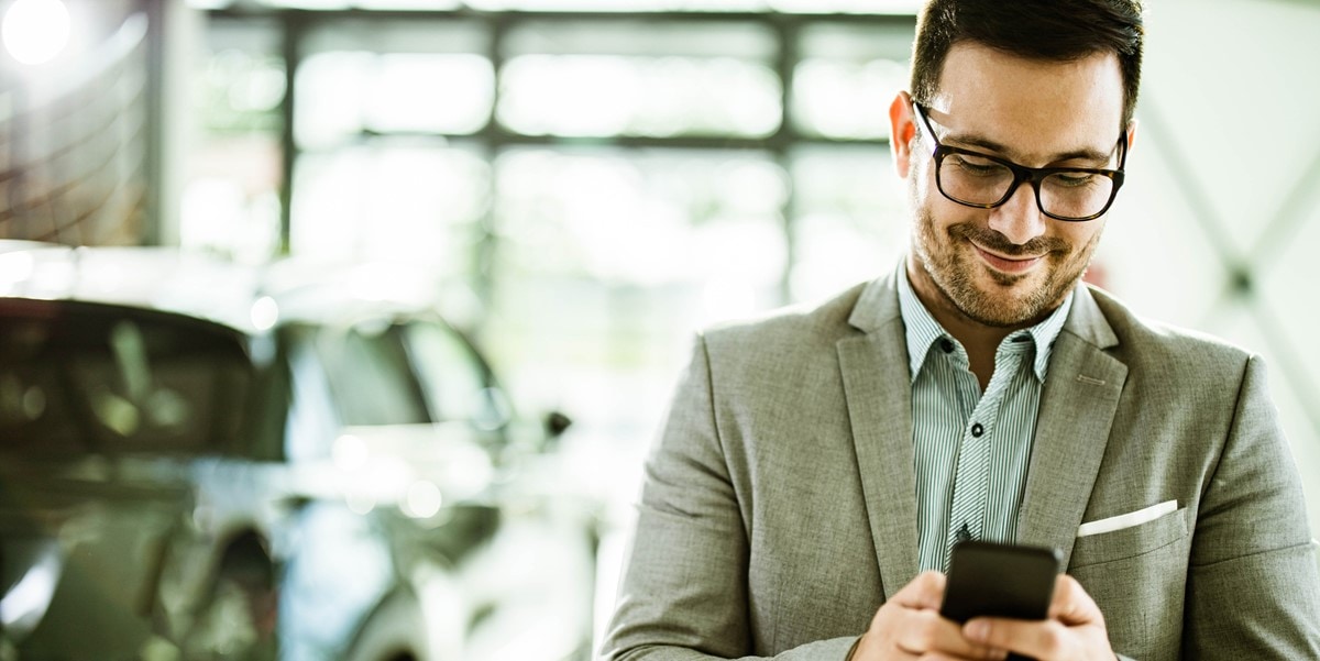 man using phone, next to car