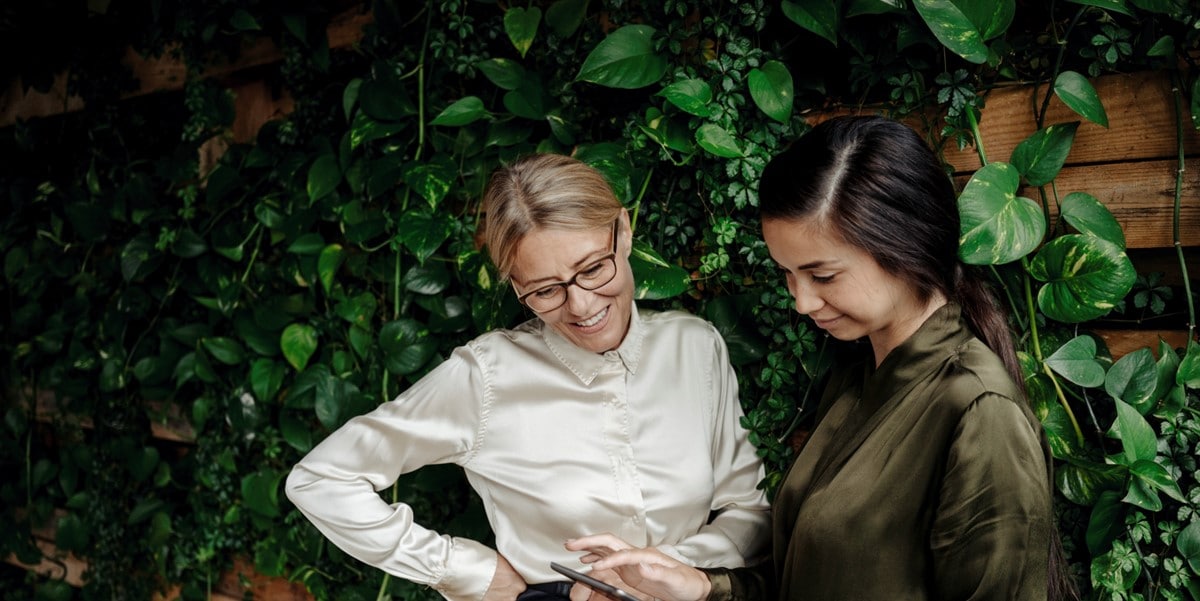 2 women looking at document in fron tof a green wall of plants