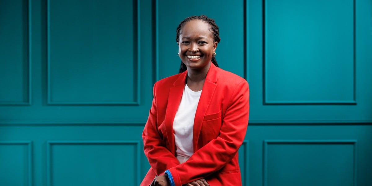 professional woman smiling, wearing a red blazer, sitting in front of teal wall