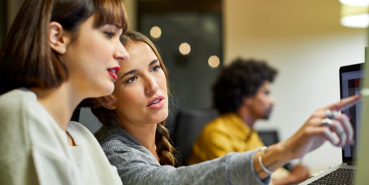 two women talking and working together next to a computer