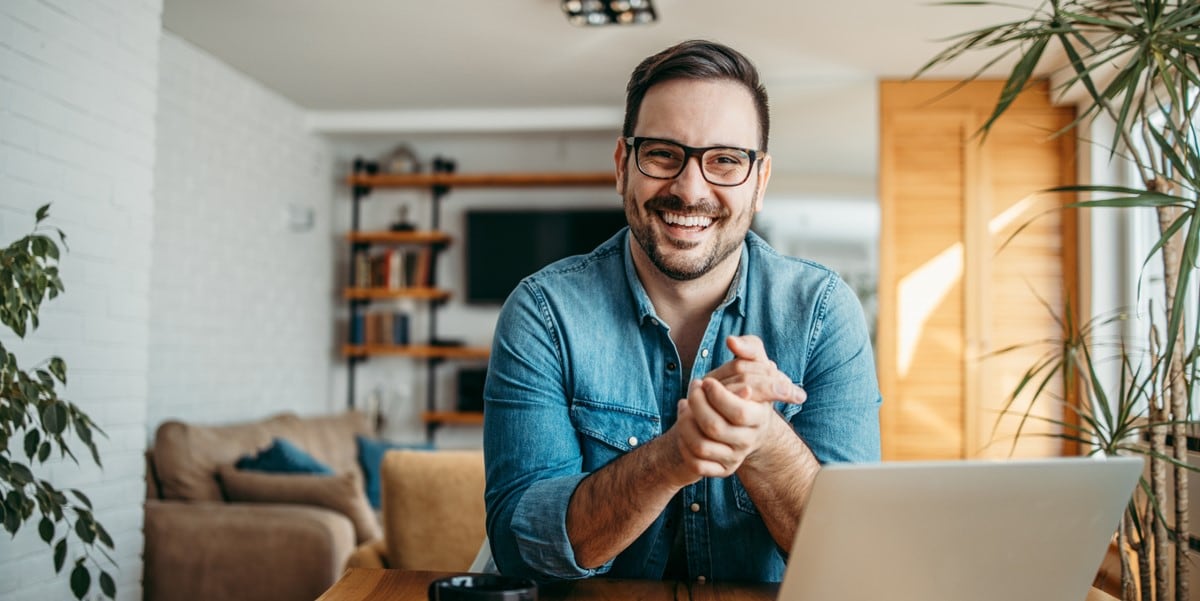 man smiling, sitting at a desk with laptop