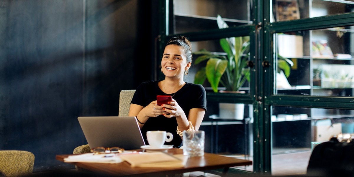woman in the office, sitting at desk using laptop and cellphone