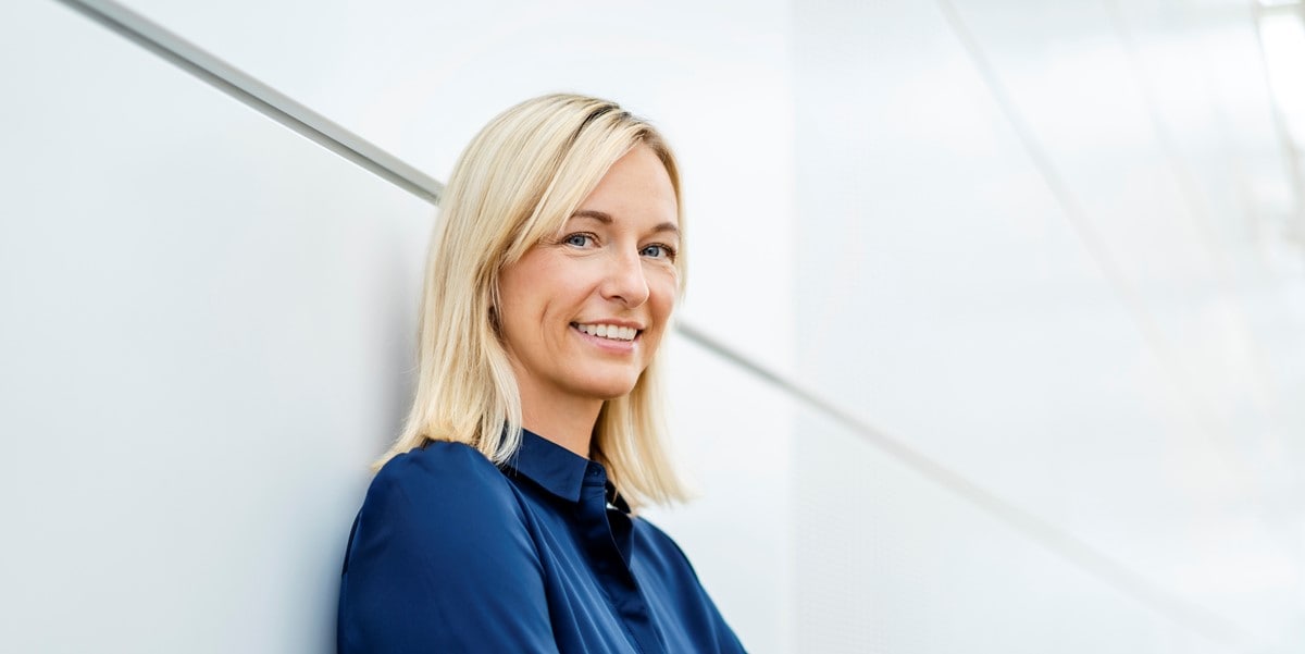 professional woman smiling, standing in front of white wall