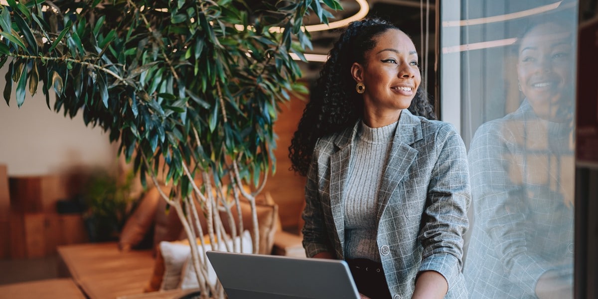 professional woman in the office, looking out window, laptop in front of her