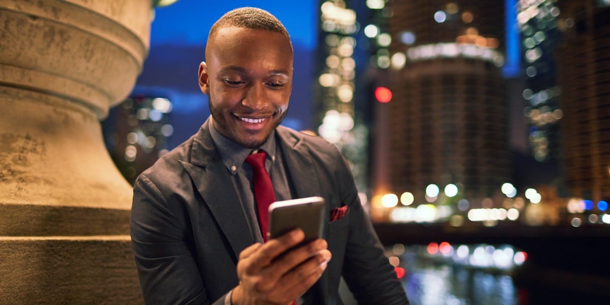 man sitting outside, looking at phone, city skyline in the background