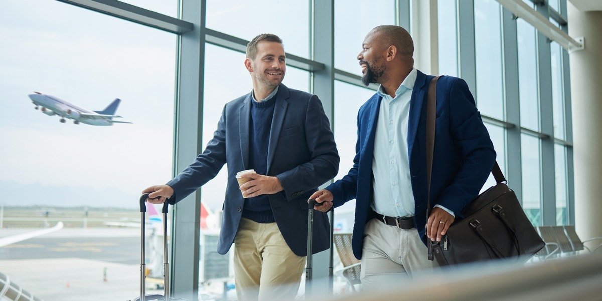 two business travelers walking through airport with luggage, airplane taking off behind them