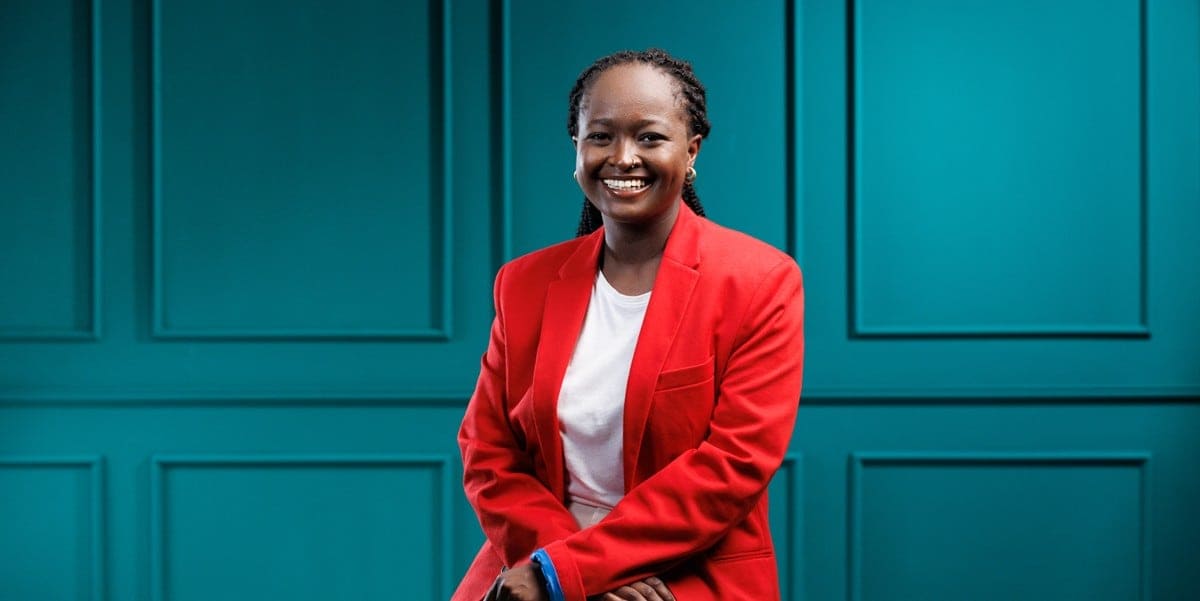 professional woman smiling, wearing a red blazer, sitting in front of teal wall