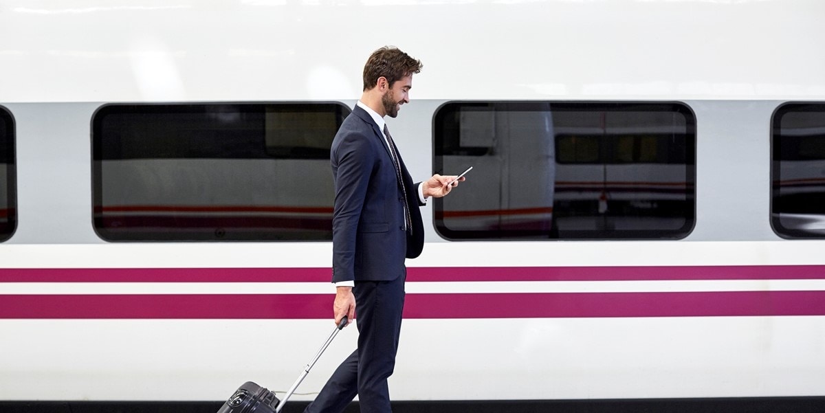 man looking at cellphone, with luggage, standing by train