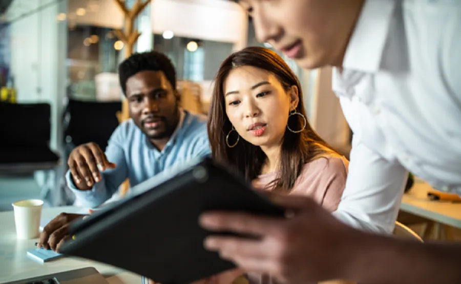 three people working in an office looking at a tablet